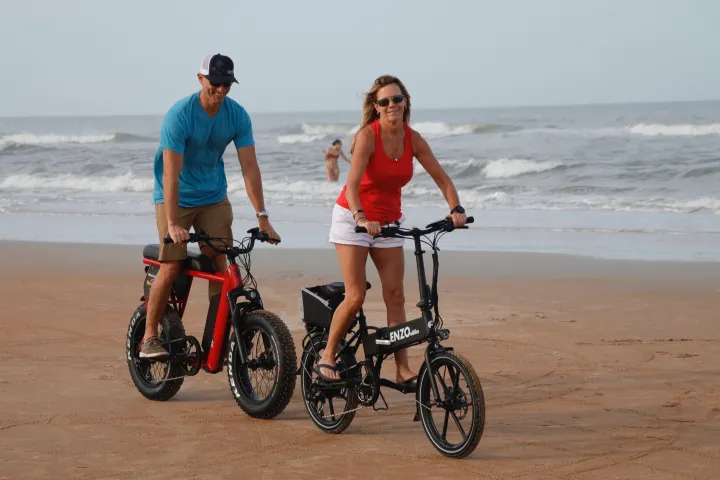 a man and woman riding ebikes on the beach